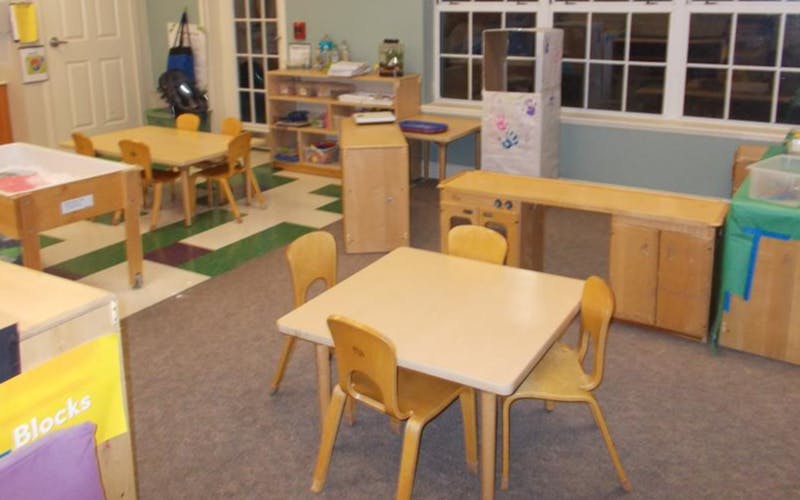 Empty classroom with small tables and chairs, shelves, and a window