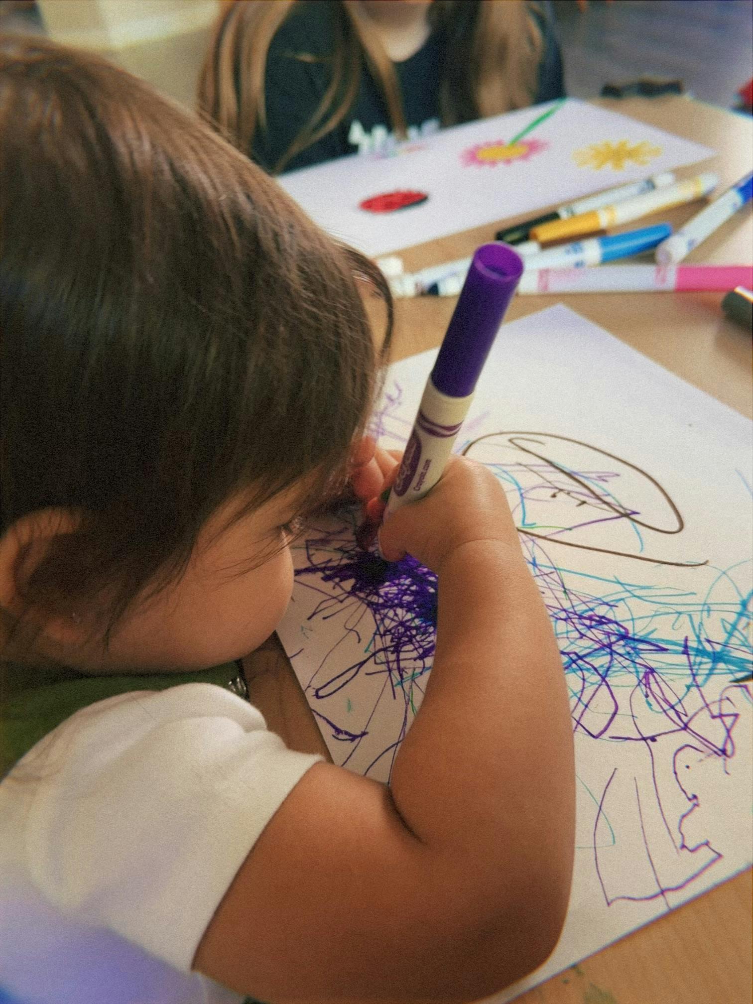 Child drawing on paper with a marker at a table