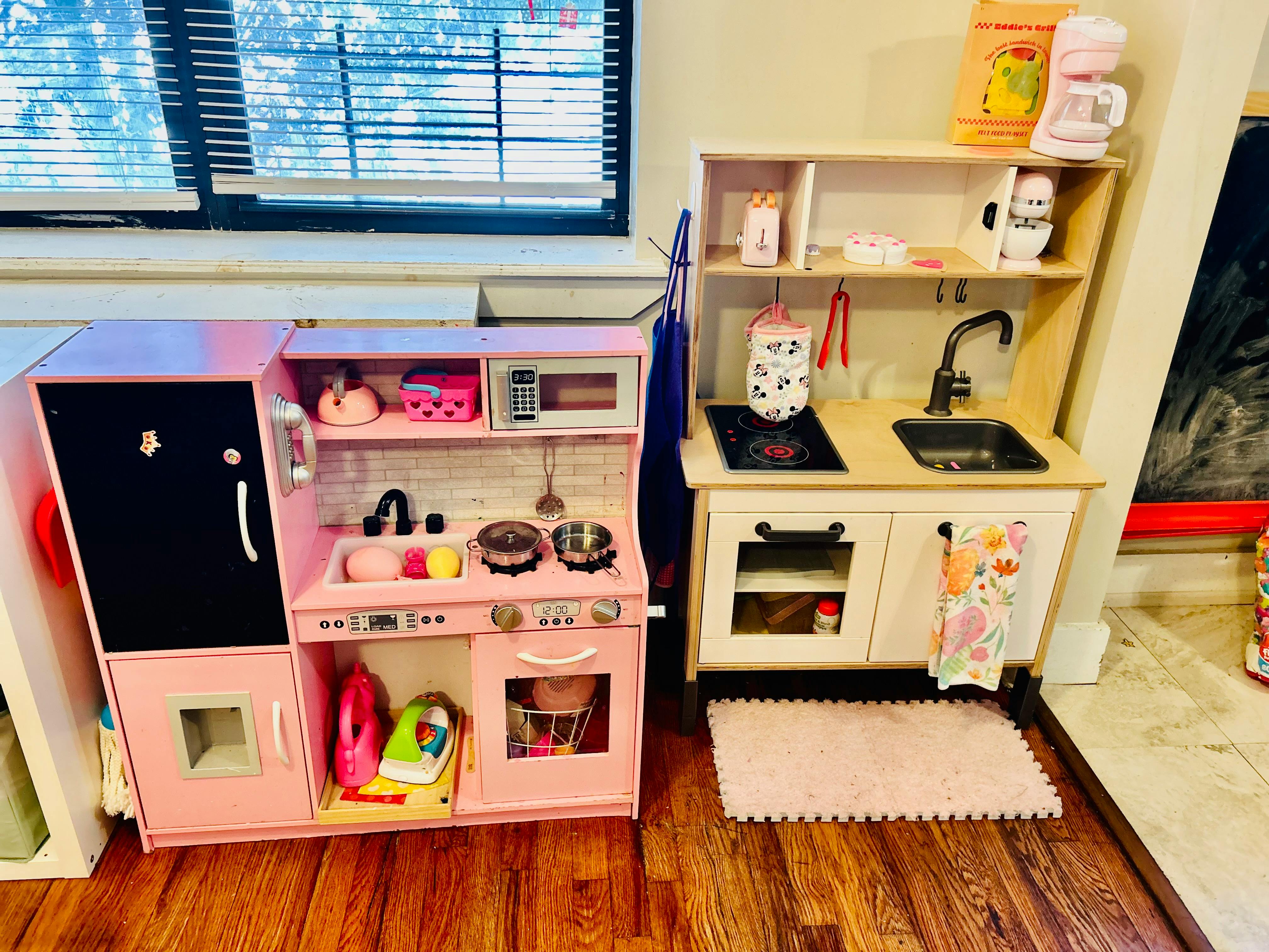 Two toy kitchens, one pink and one white, with various play accessories