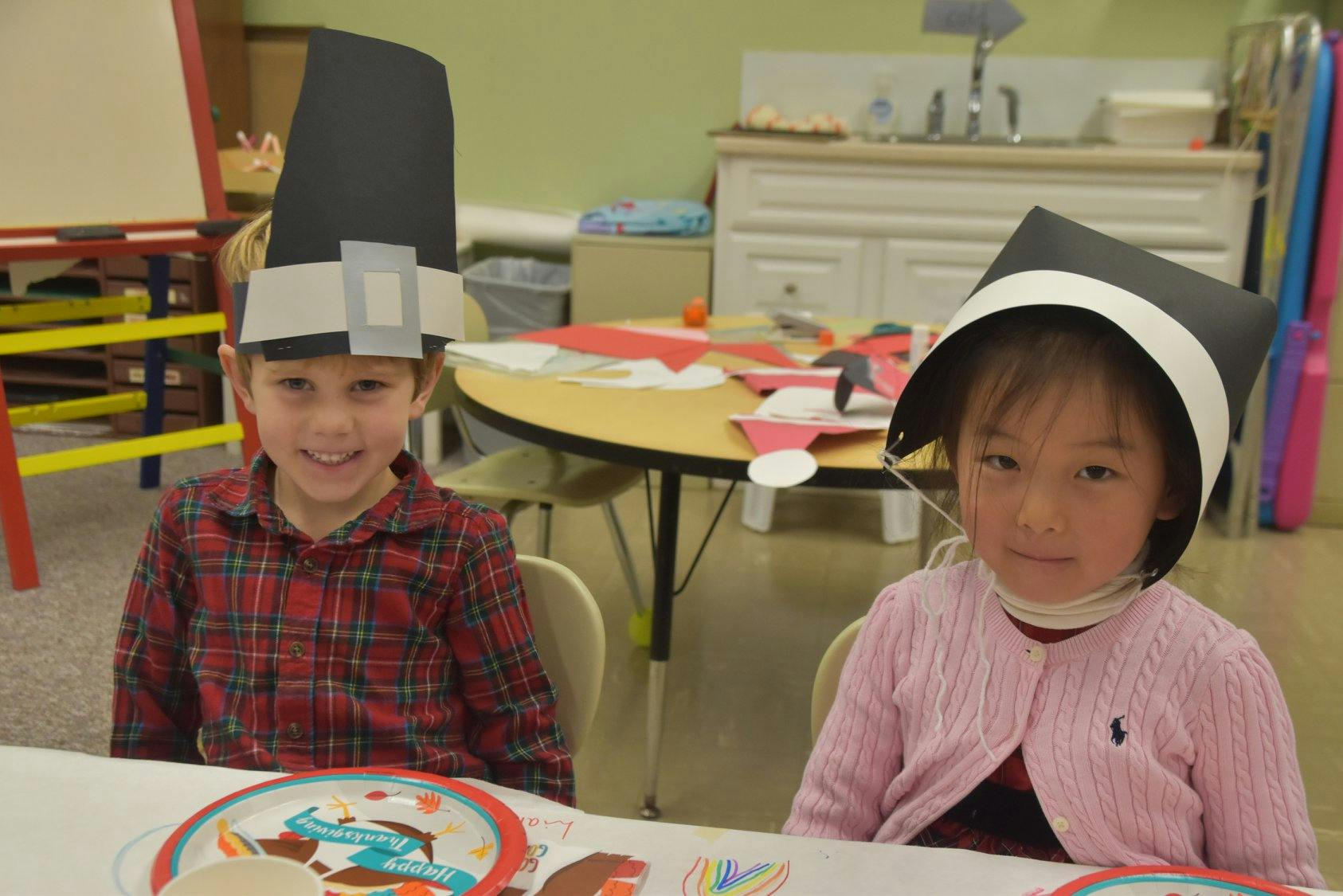 Two children wearing pilgrim hats sitting at a table
