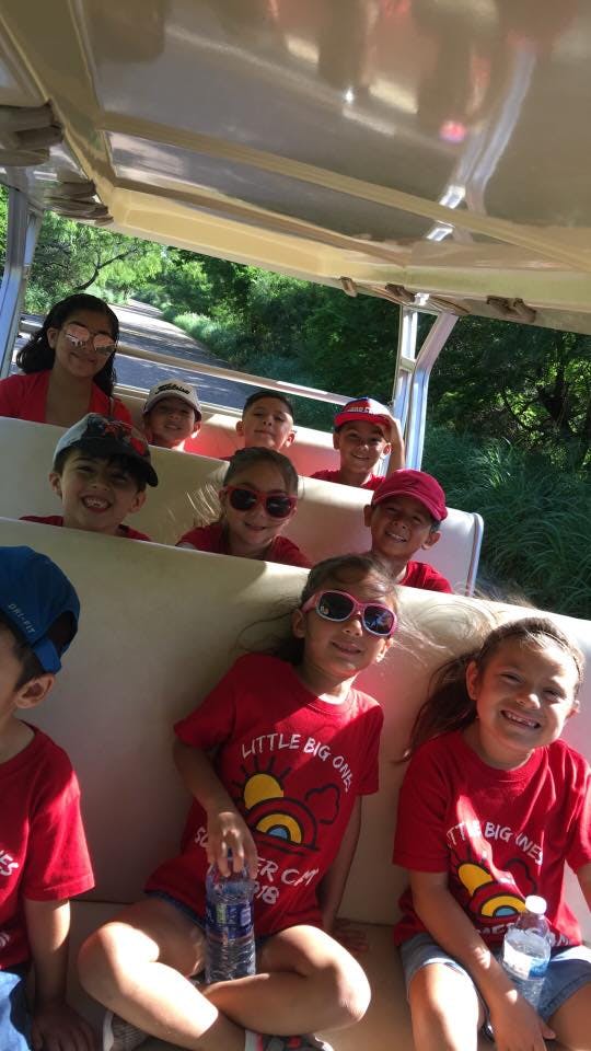 Group of children and teens in red shirts riding in an open-air vehicle