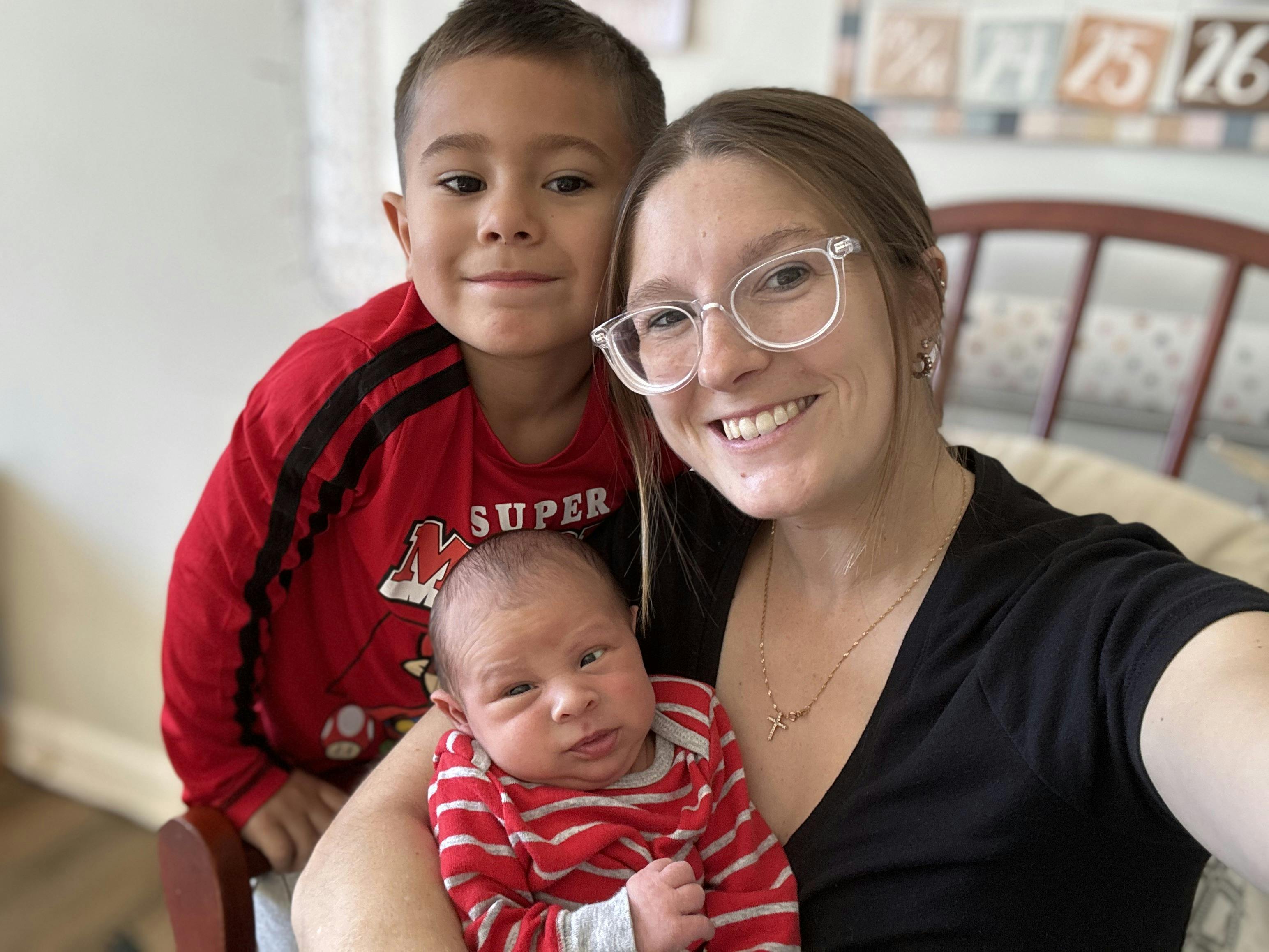 Person holding a baby, with a child standing behind them