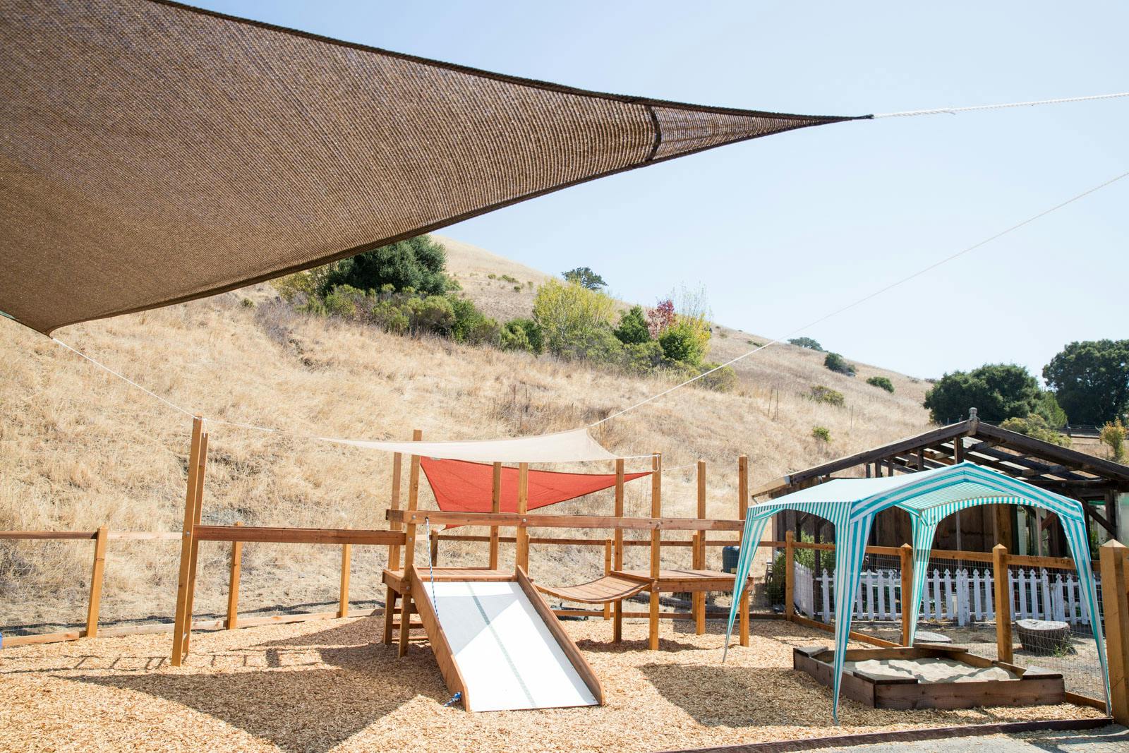 Outdoor playground with slide, wooden structures, and shade sails