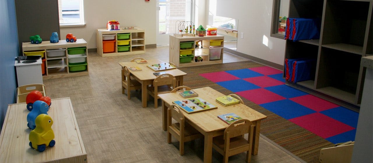 Classroom with small tables and chairs, storage units, and a checkered mat