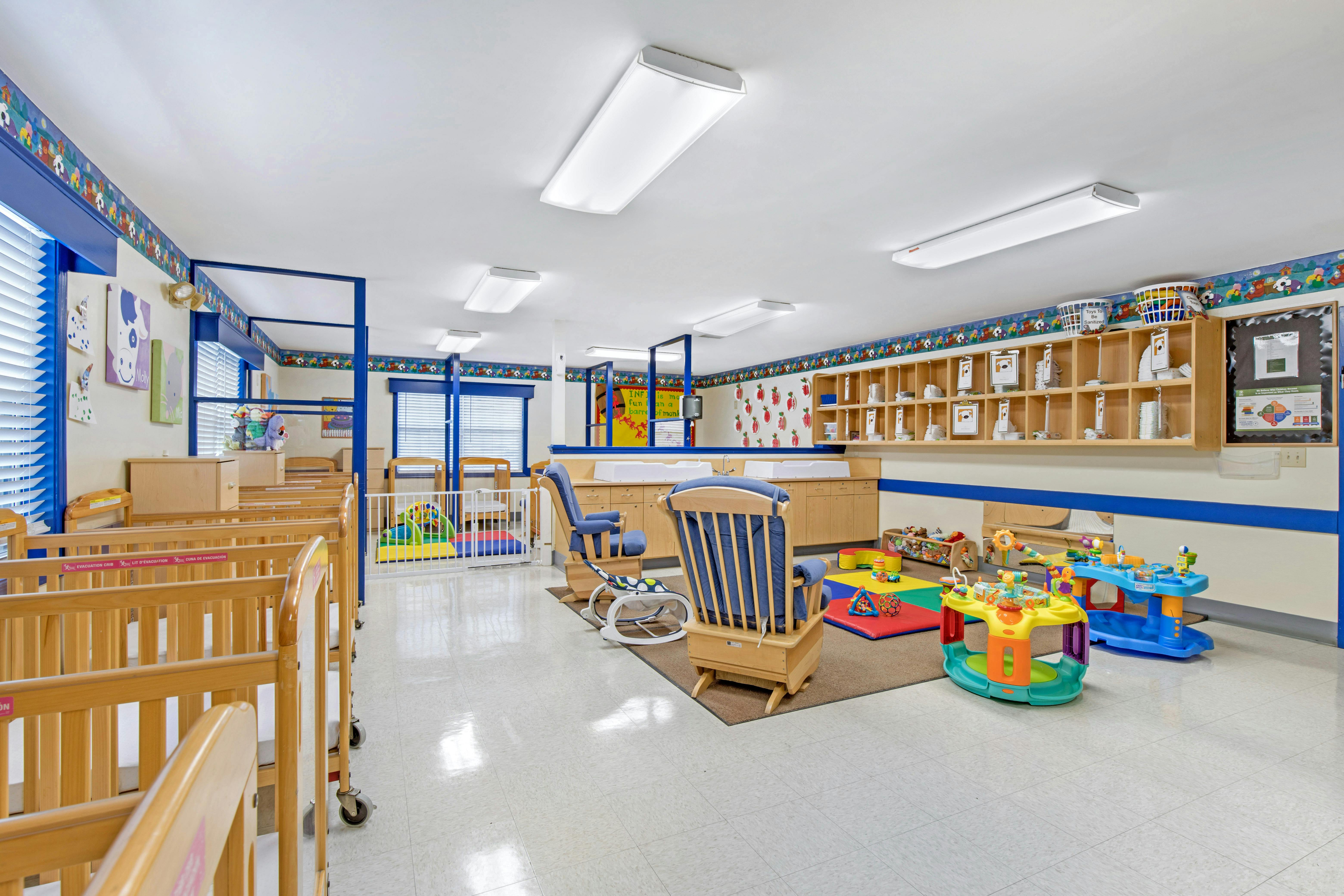cribs, rocking chairs, and play mats in a child care room