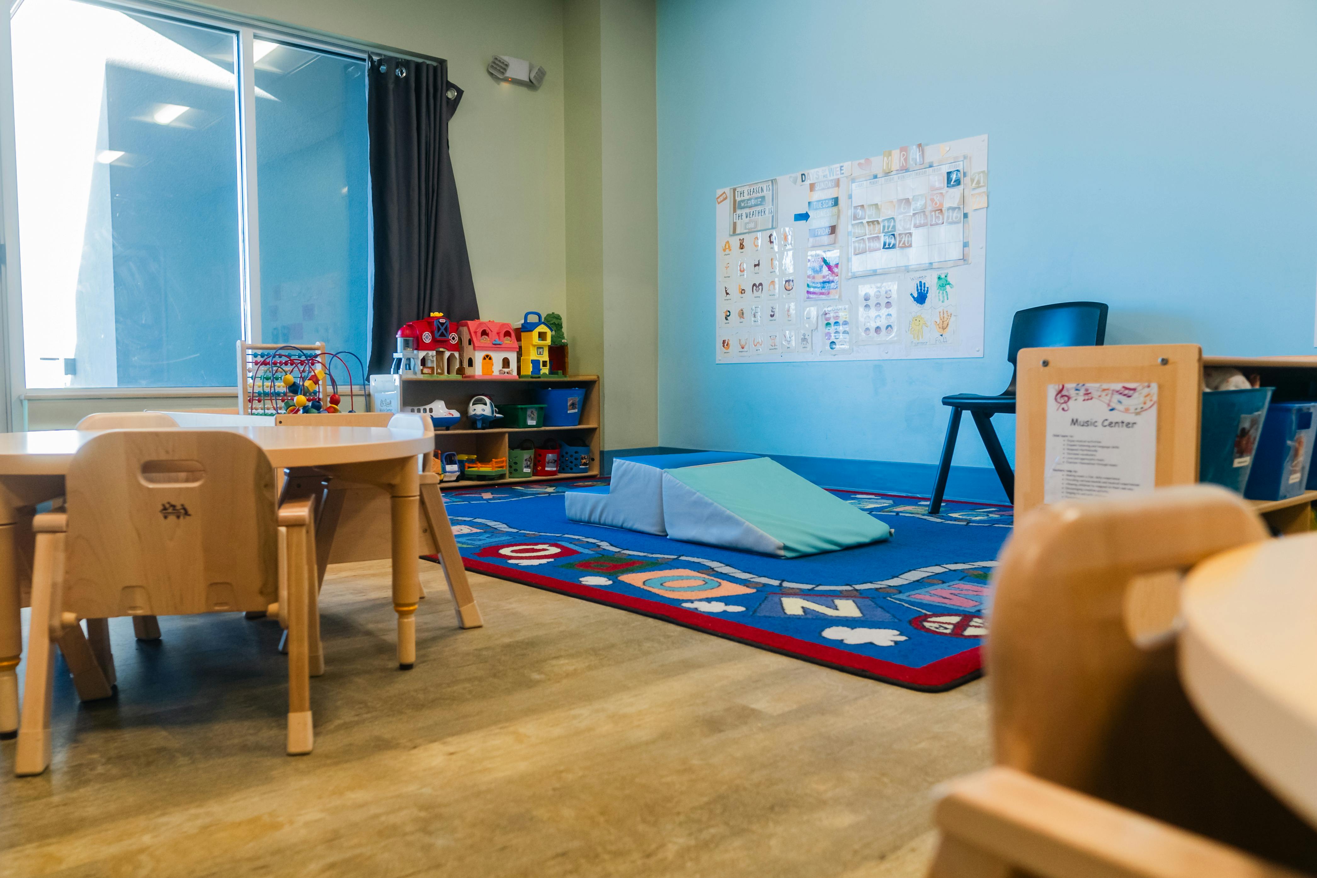 Classroom with small table and chairs, play mats, and a colorful rug