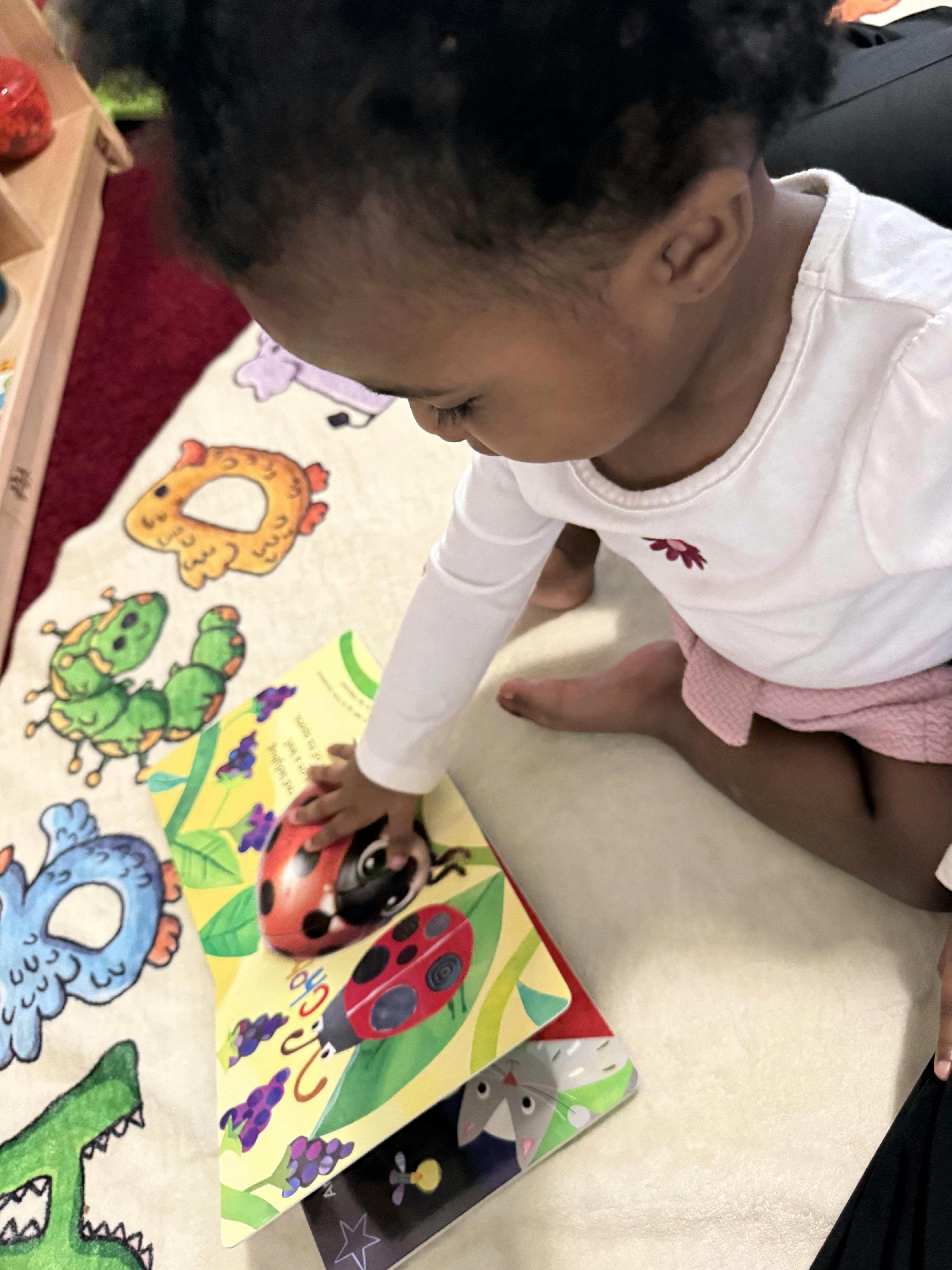 Child on a mat reaching for a book with a ladybug on the cover
