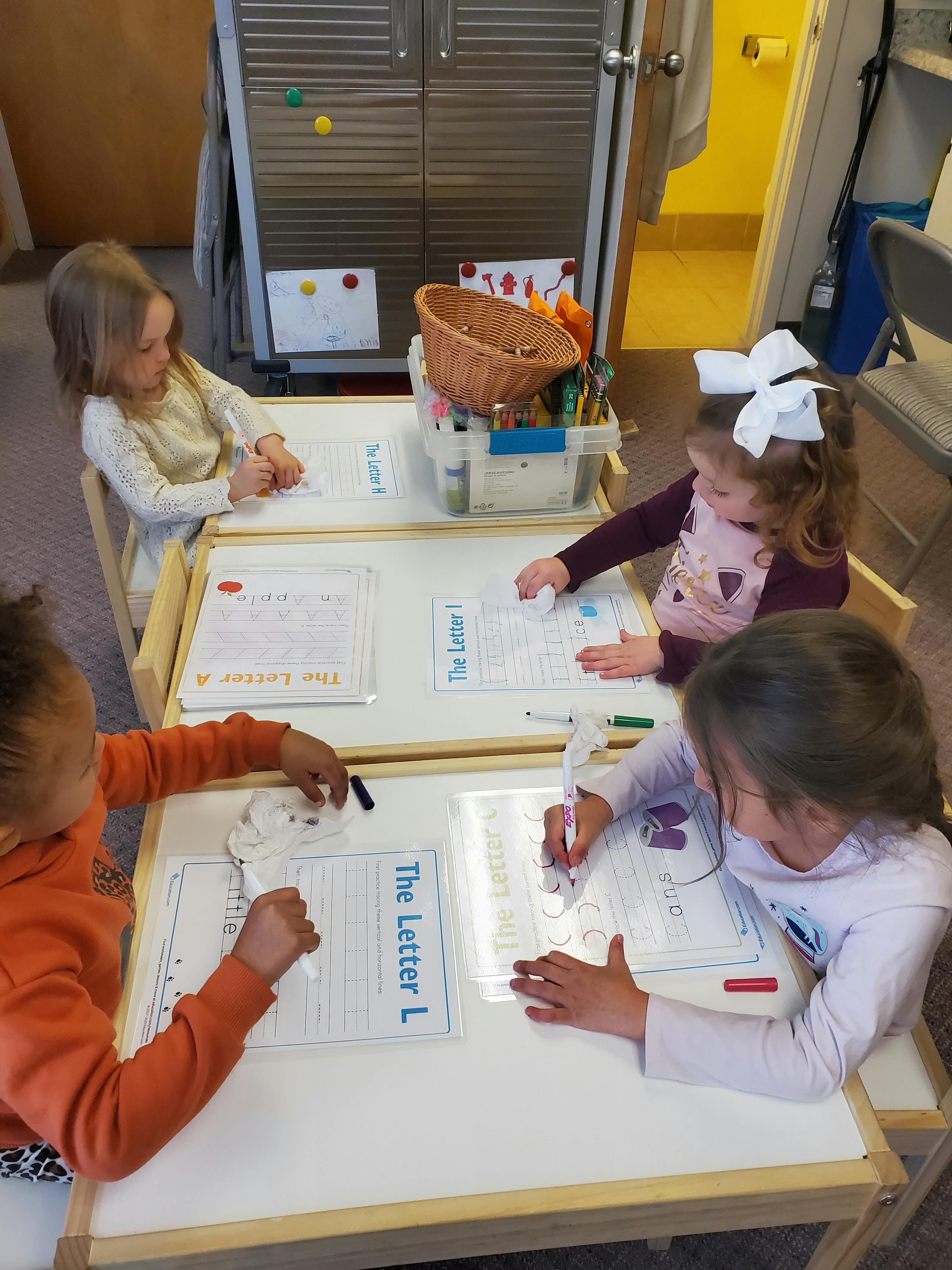 Four children writing on light-up boards in a classroom