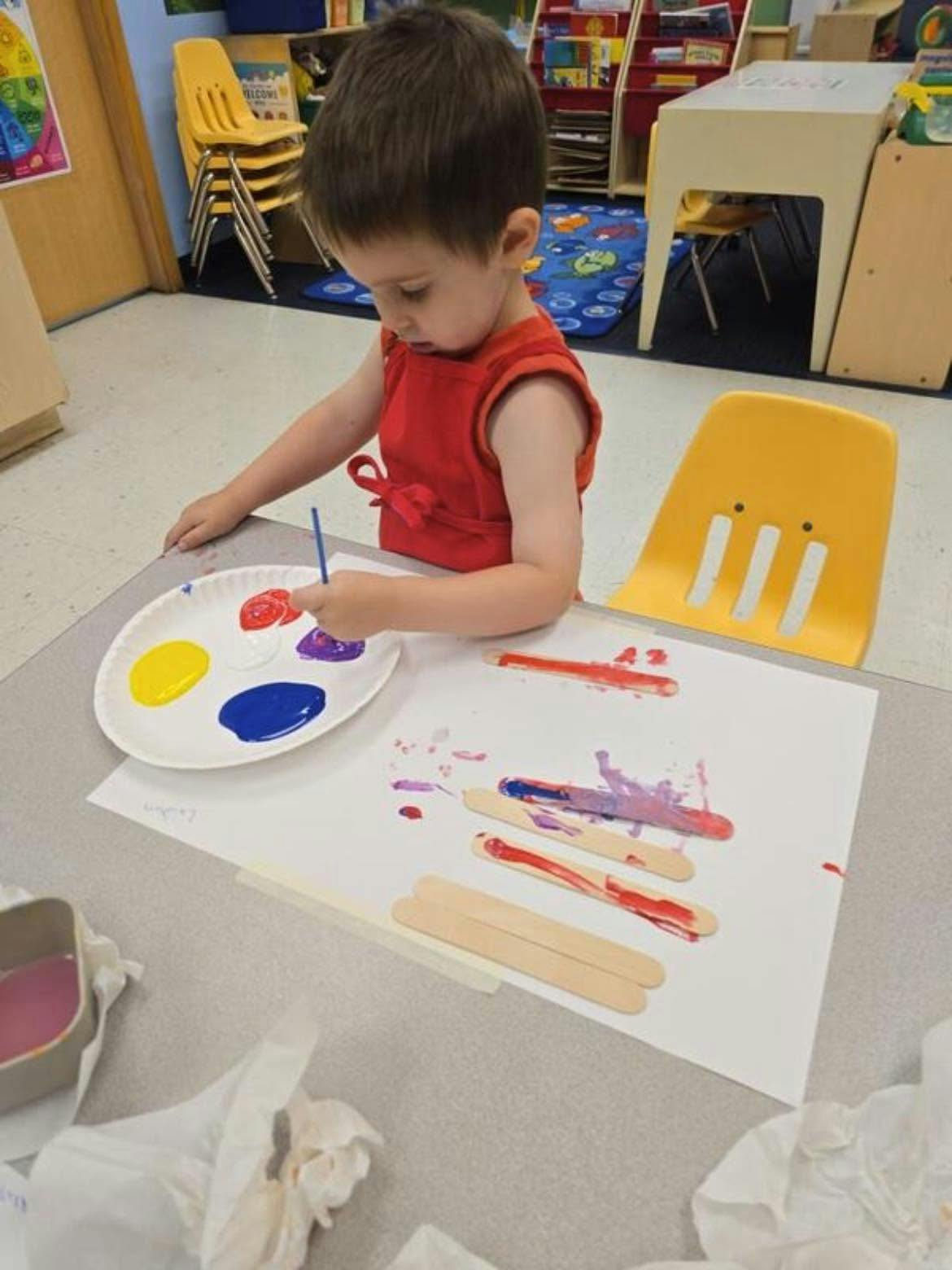 Child painting craft sticks at a table in a classroom