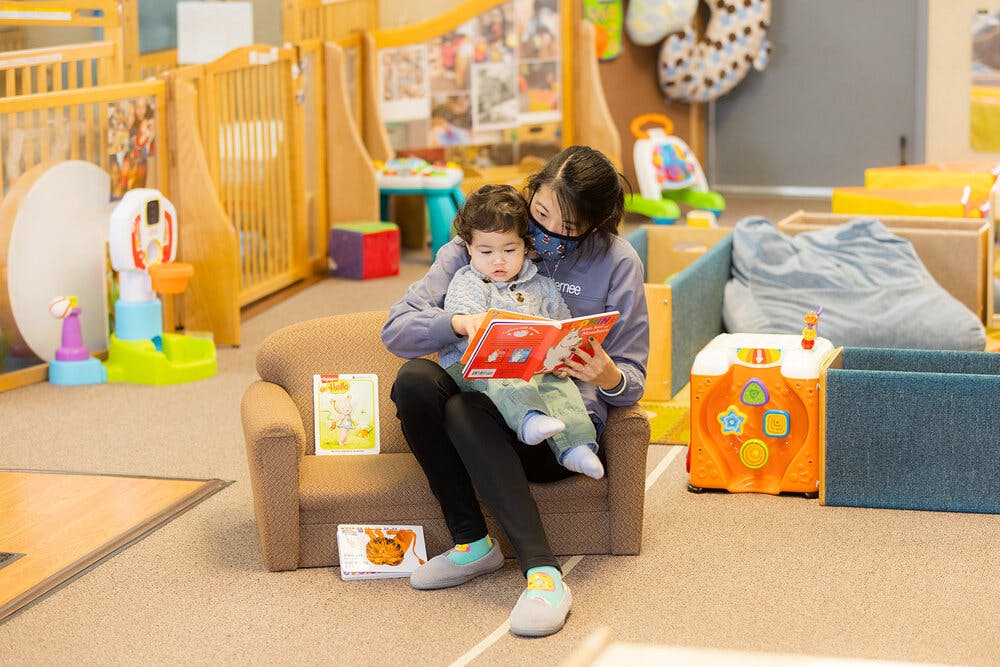 Person and child sitting on a small couch reading a book