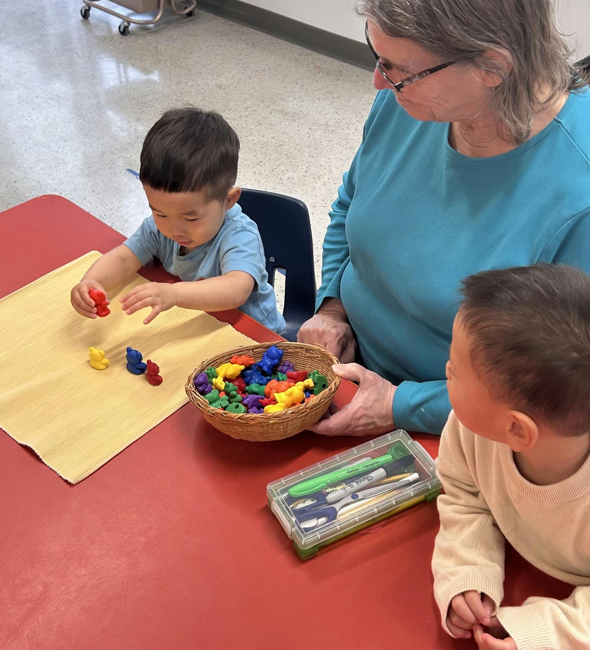 Adult and two children playing with colorful bear-shaped counters at a red table
