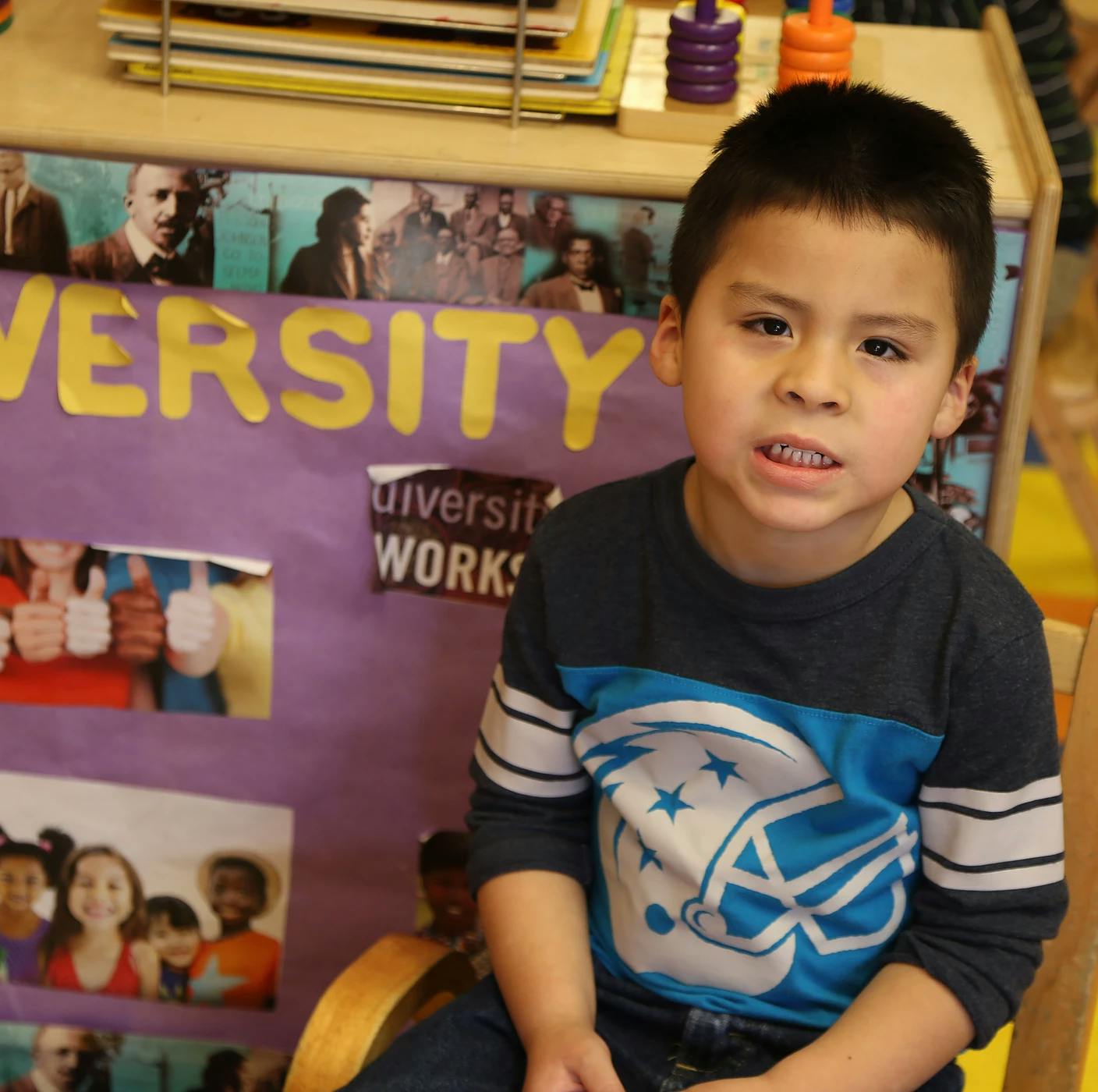 Child sitting in front of a purple board with "DIVERSITY" written on it