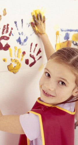 Child making handprints on a wall with paint