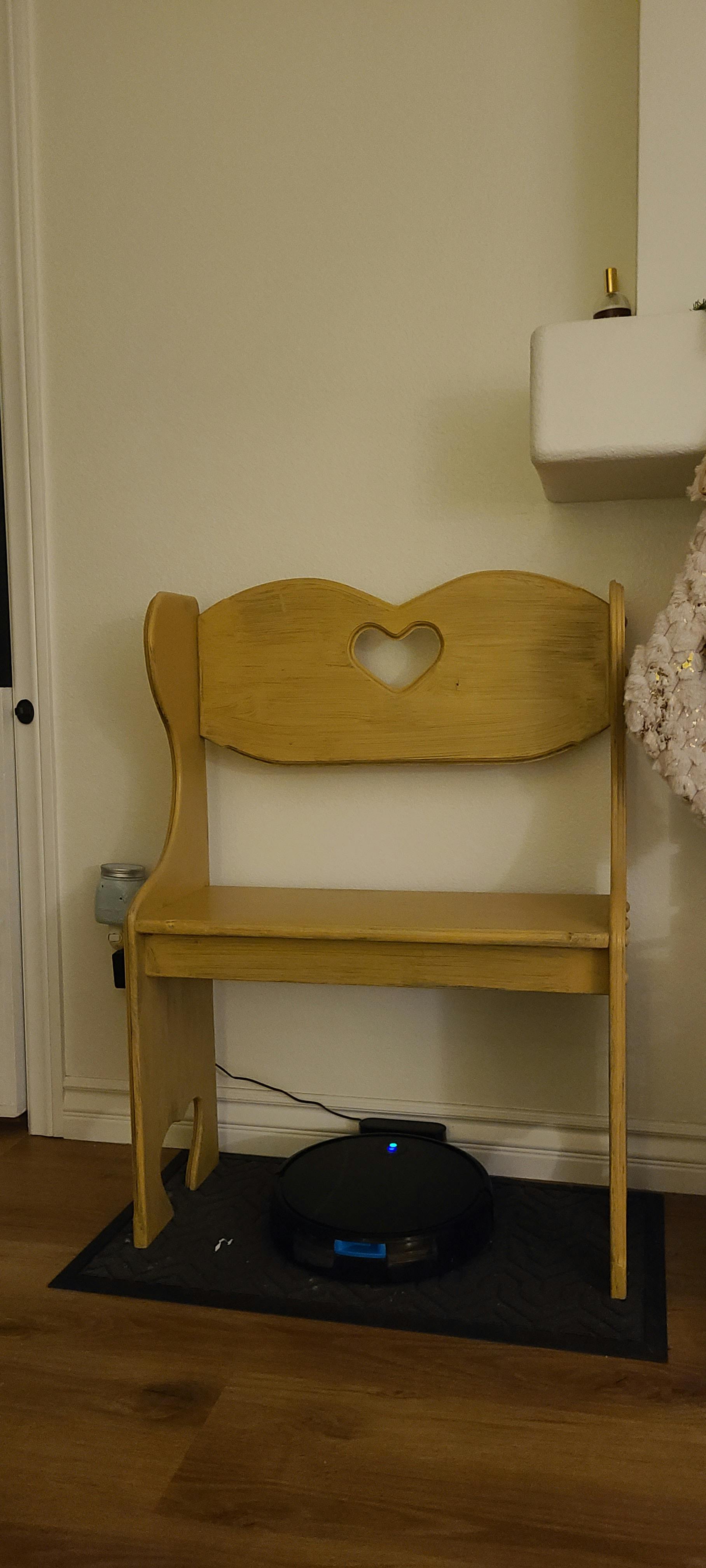 Wooden bench with a heart cutout in the backrest, robot vacuum underneath