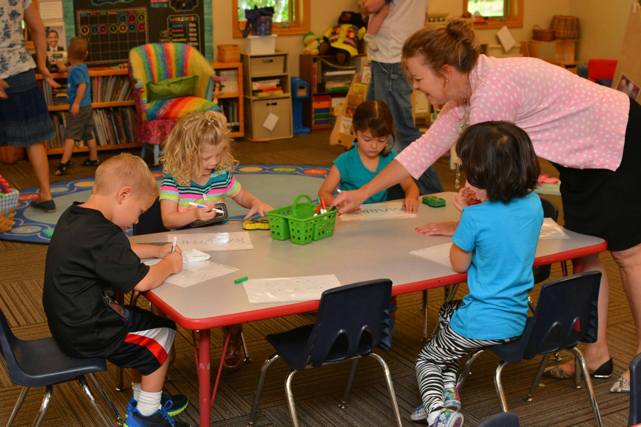 Adult and children drawing at a table in a classroom