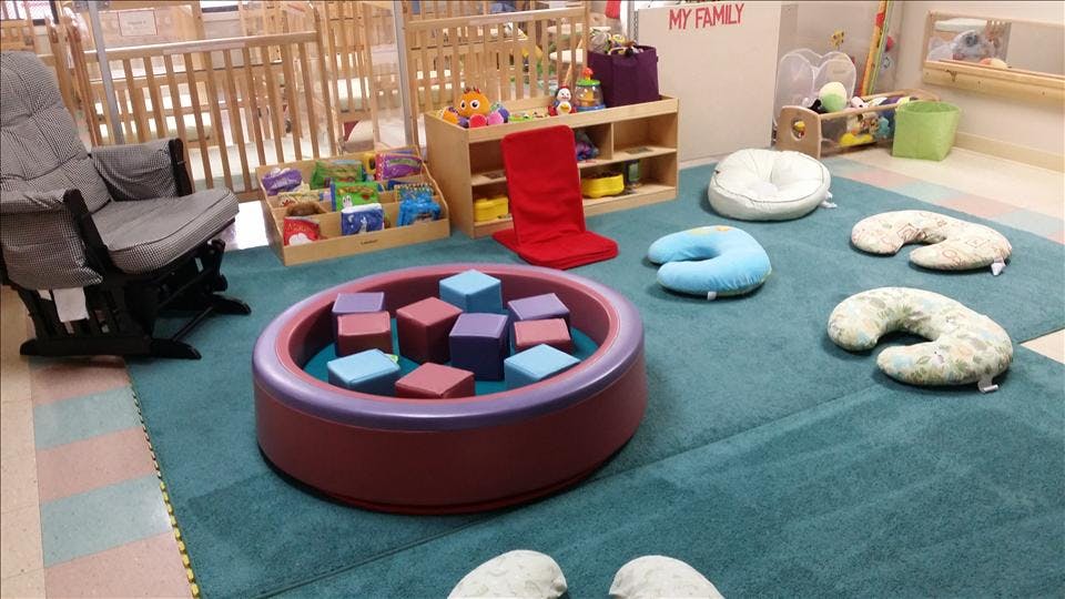 baby nursery with cribs, play mat, chair, pillows, and soft blocks