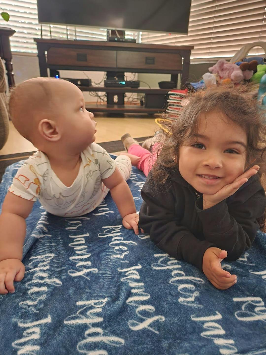 Baby on stomach looking left, child on stomach looking forward