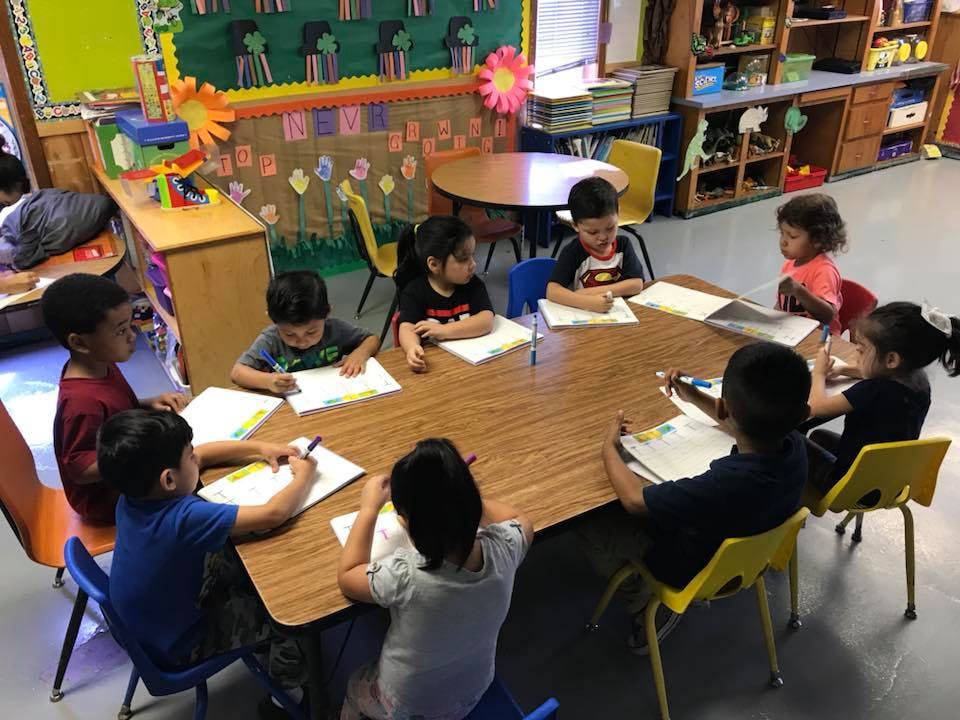 Children sitting around a table in a classroom, writing on papers