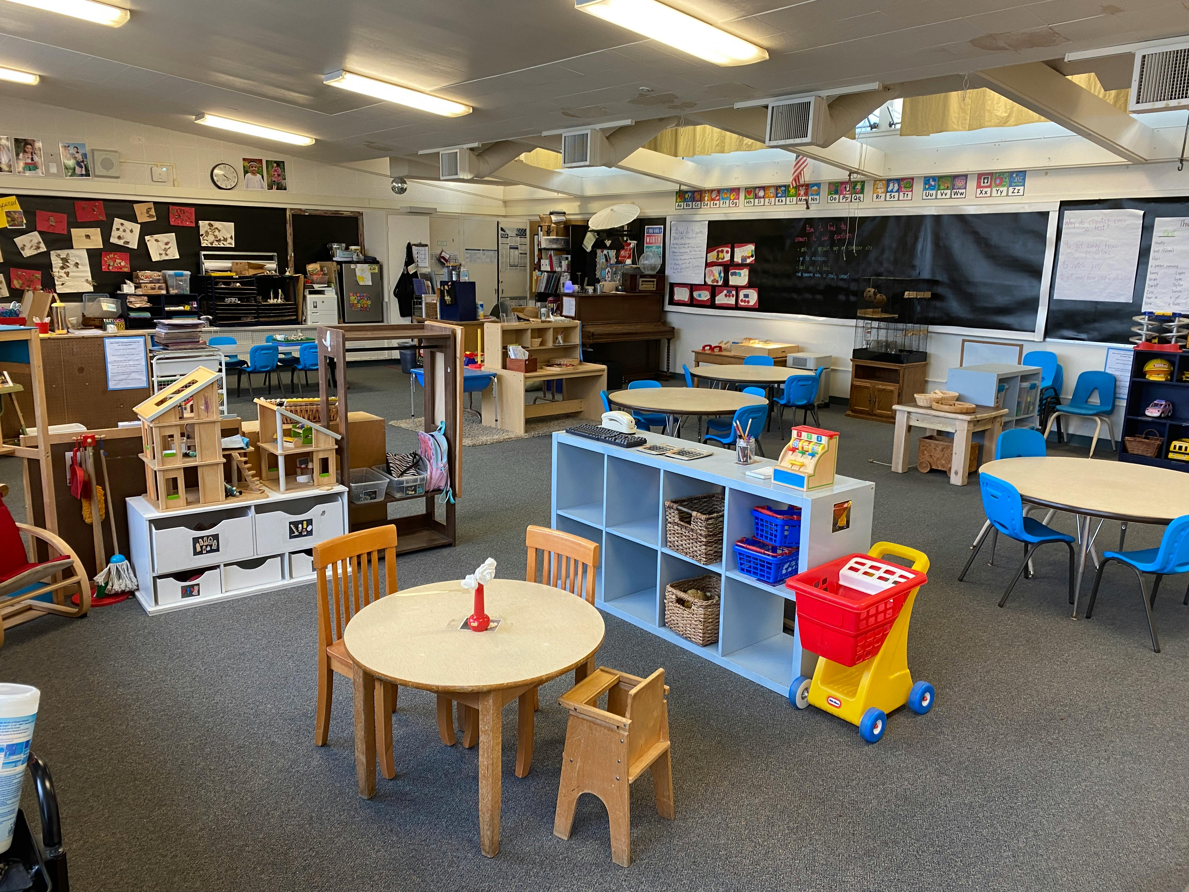 Empty classroom with small tables and chairs, shelves, and toys