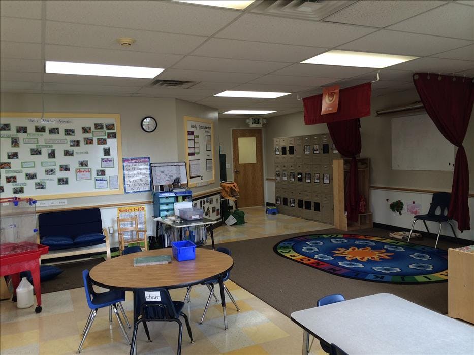 An empty classroom with tables, chairs, and a colorful rug on the floor