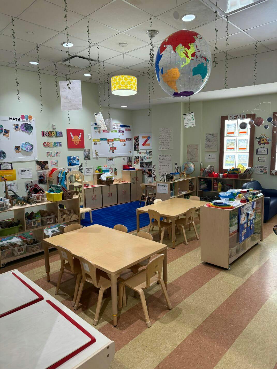 Colorful classroom with child-sized tables and chairs, shelves, and a large globe