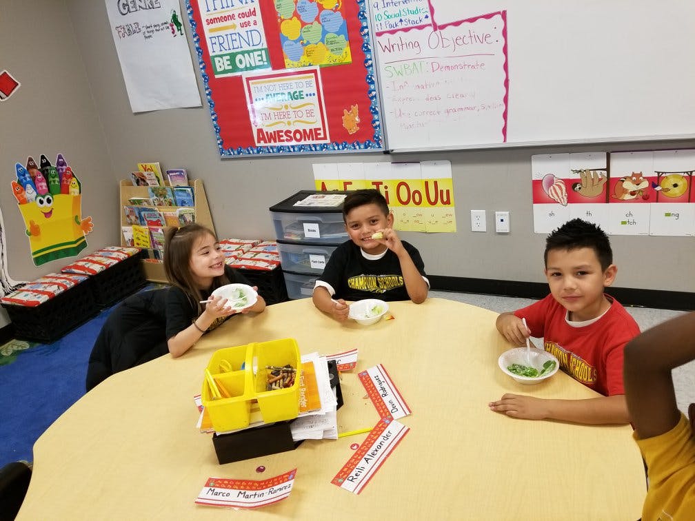 Three children eating from bowls at a round table in a classroom