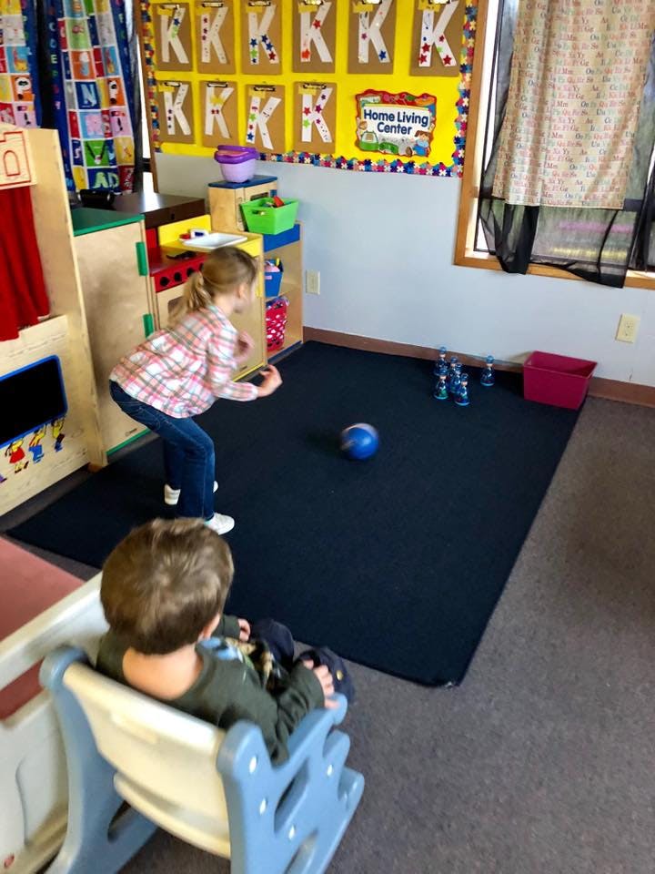 Child bowling with a blue ball and pins in a classroom