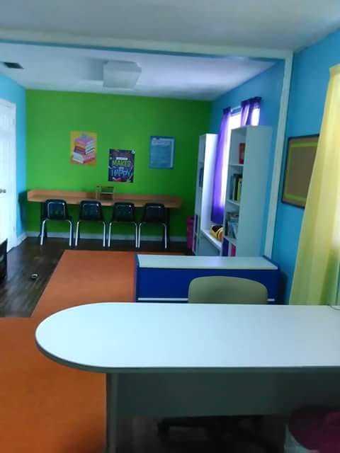 Classroom with green and blue walls, tables, chairs, and bookshelves