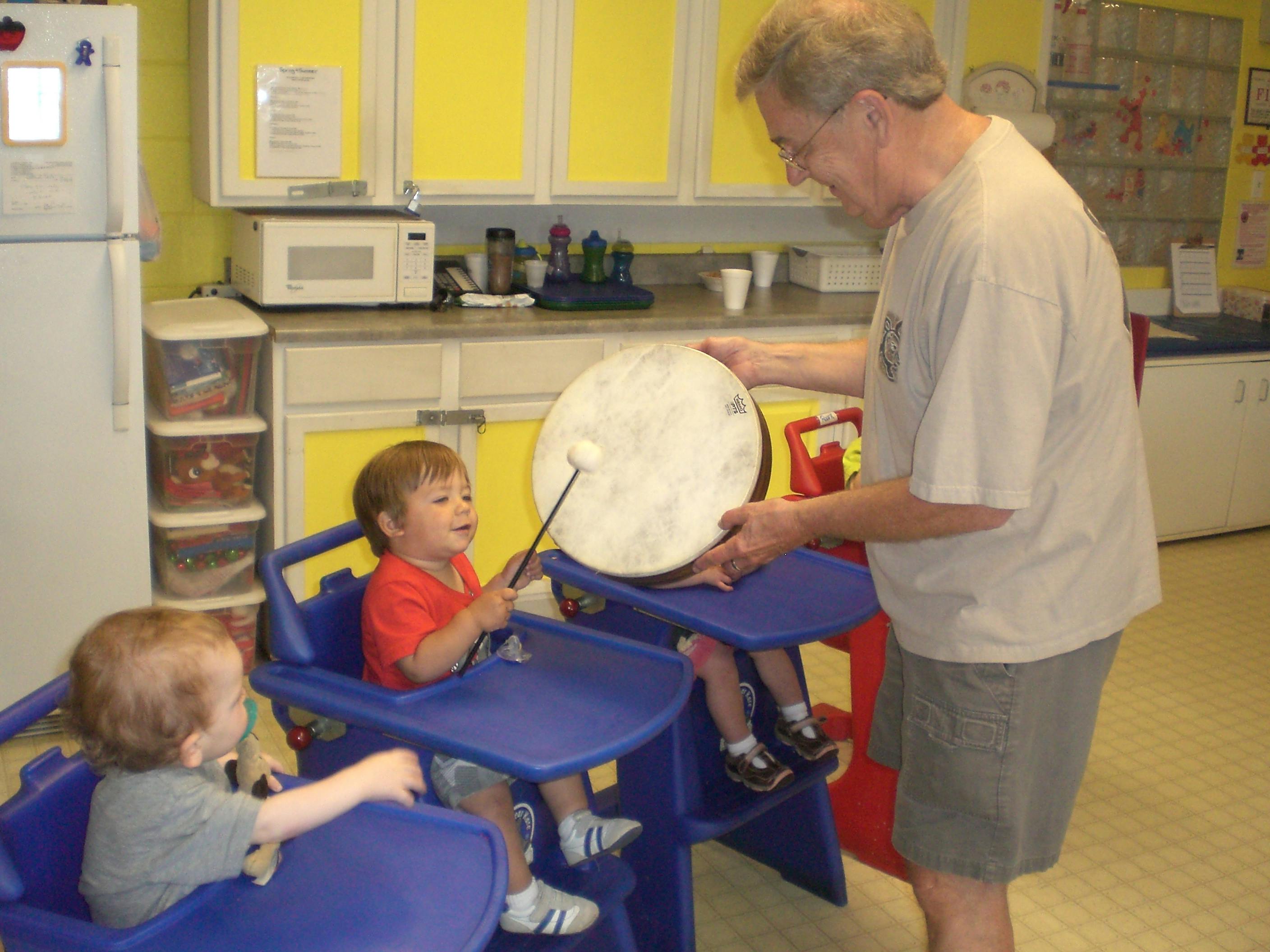 Adult holding a drum for a child in a high chair to play
