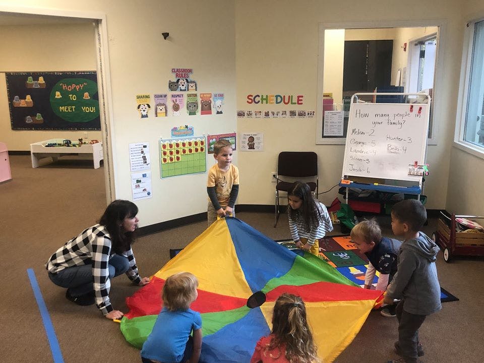 Adult and children playing with a colorful parachute in a classroom