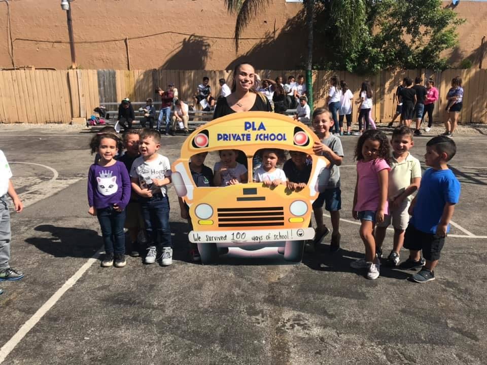 Adult and children posing with a school bus cutout that says "PLA Private School"