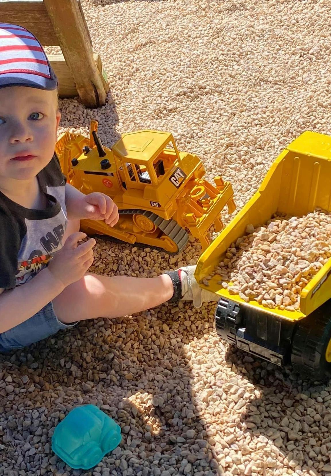 Child playing with toy construction vehicles in gravel