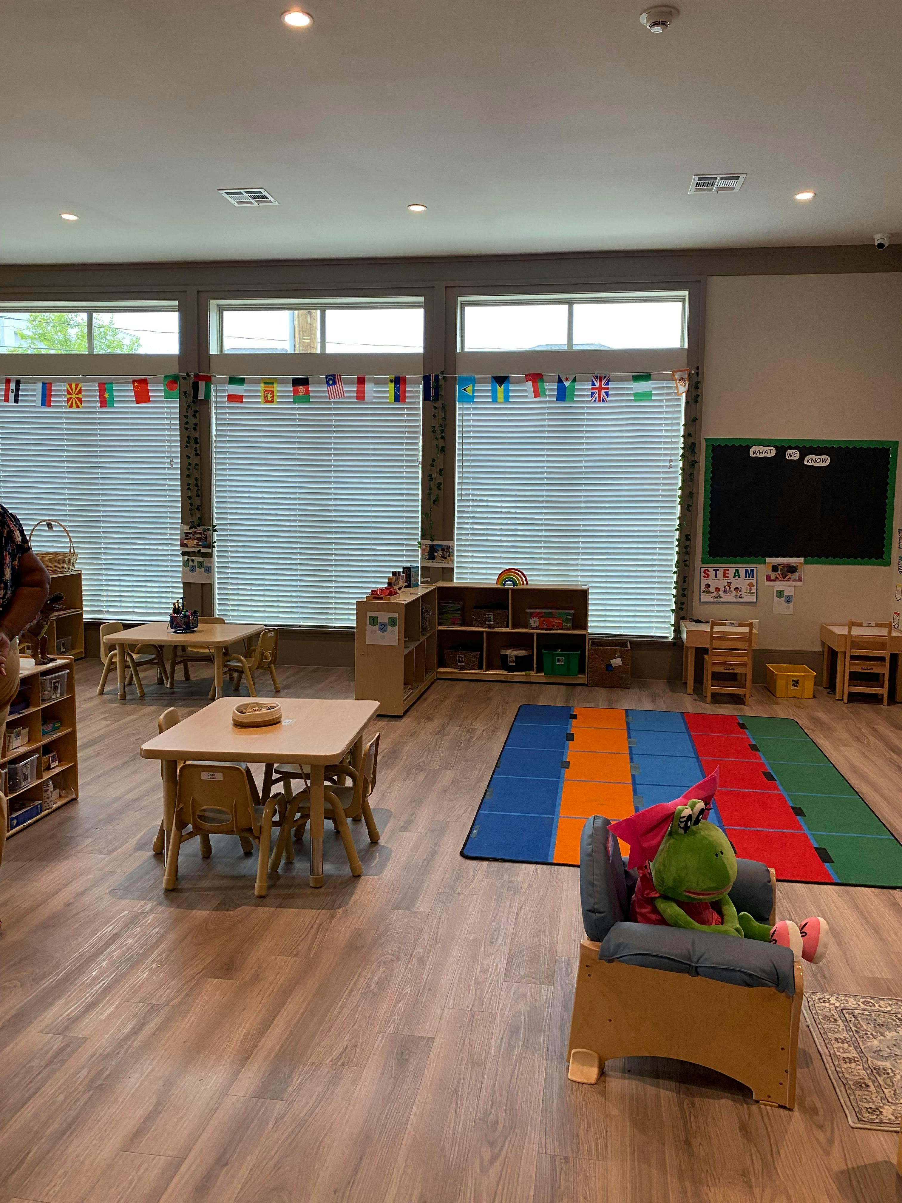 Classroom with small tables and chairs, colorful rug, and windows