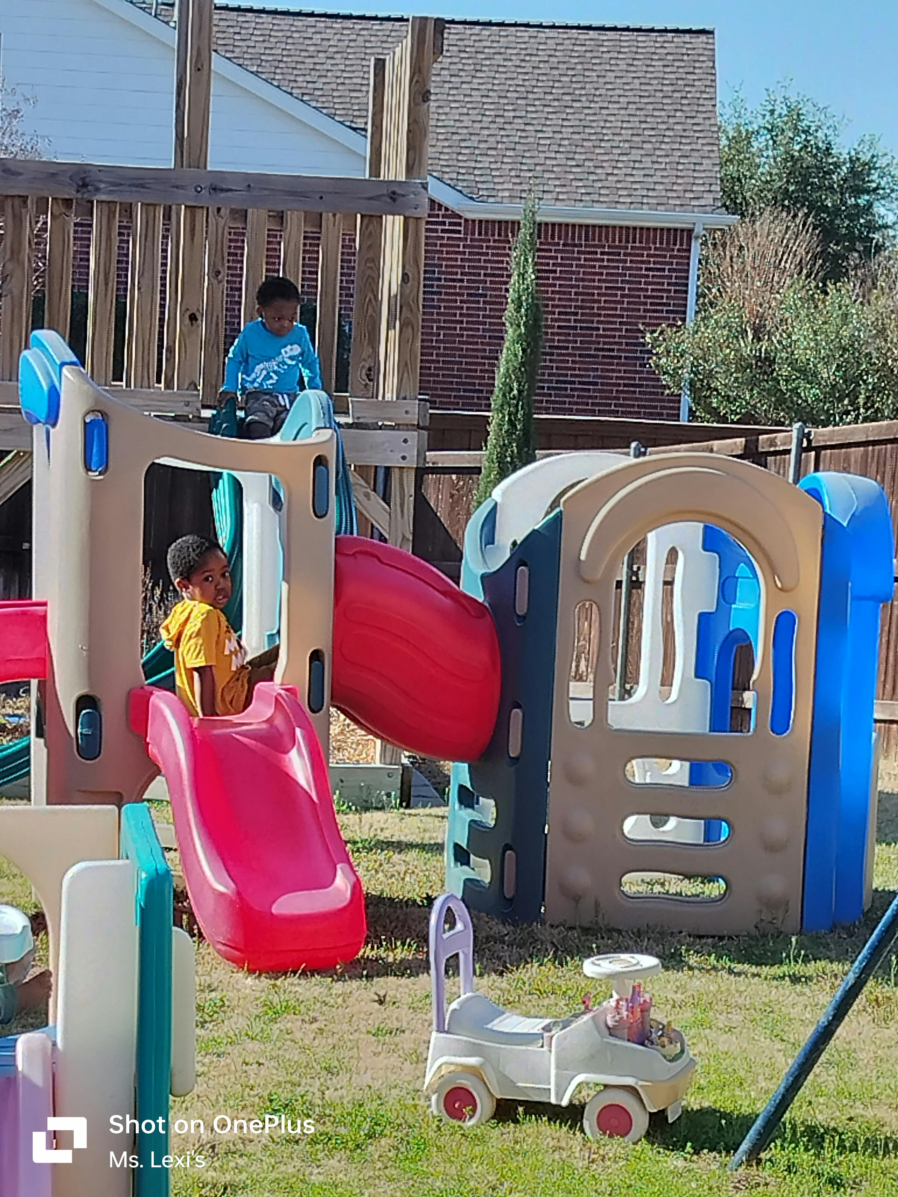 Two children playing on a colorful outdoor playset with slides
