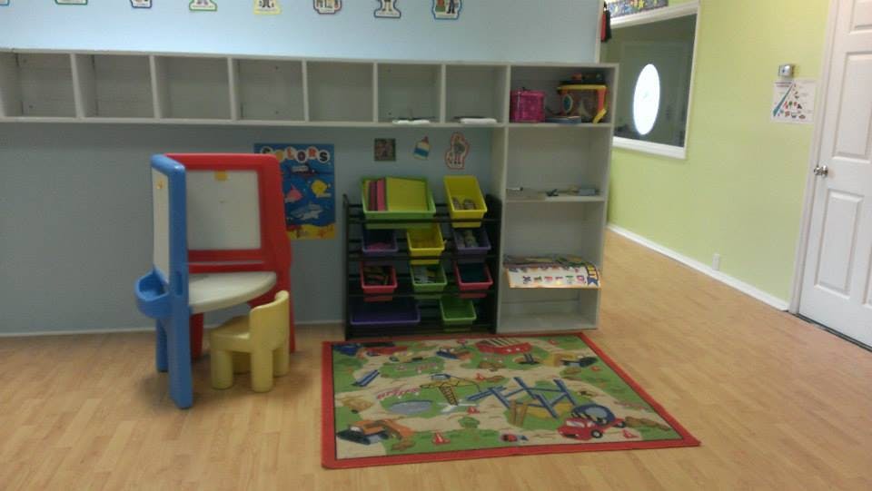 Child's easel and chair in a classroom with shelves and a play rug