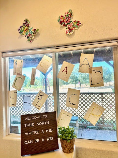 Window with alphabet cards and a sign that reads "WELCOME TO TRUE NORTH WHERE A KID CAN BE A KID"
