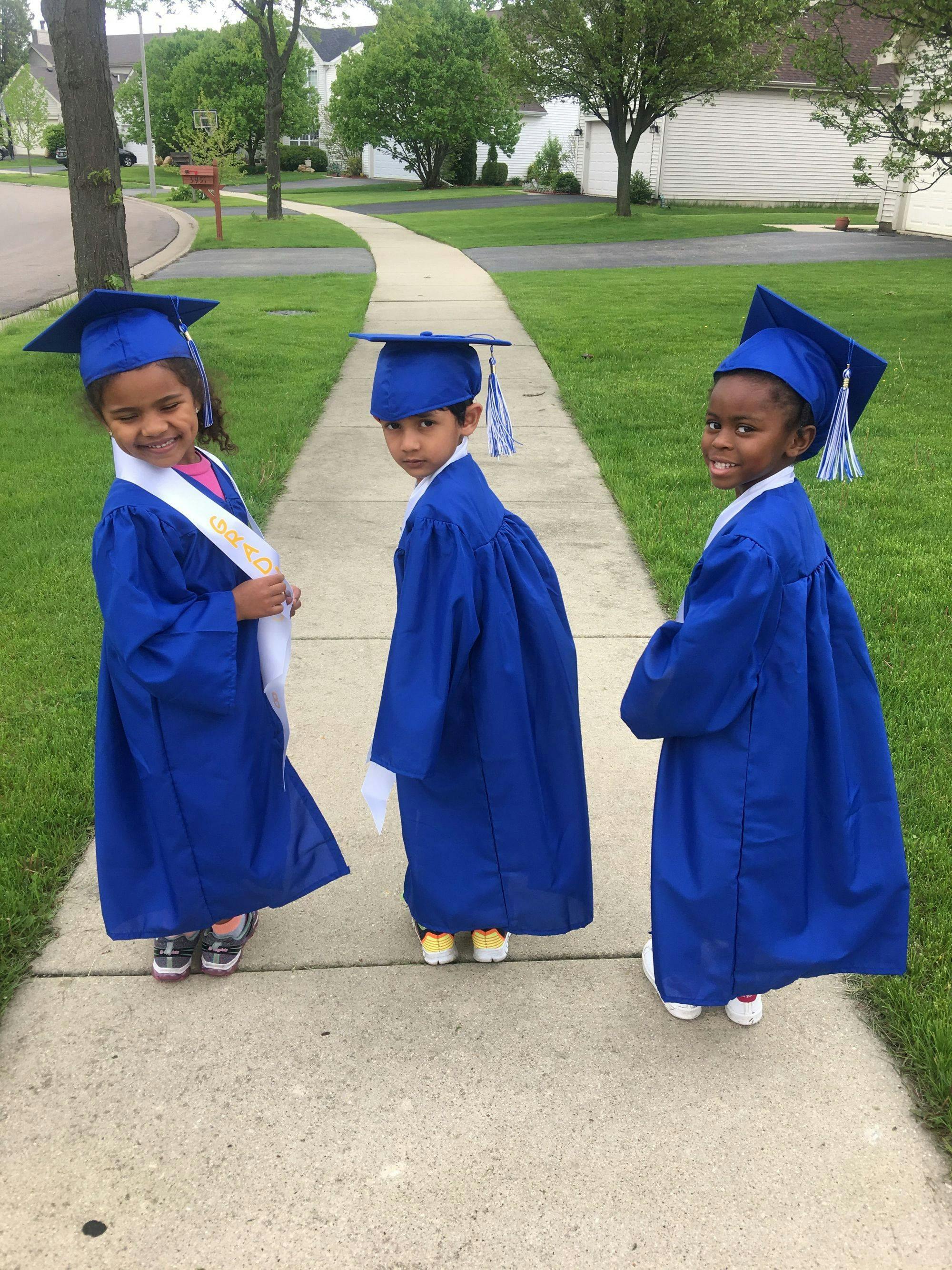 Three children in blue graduation caps and gowns on a sidewalk