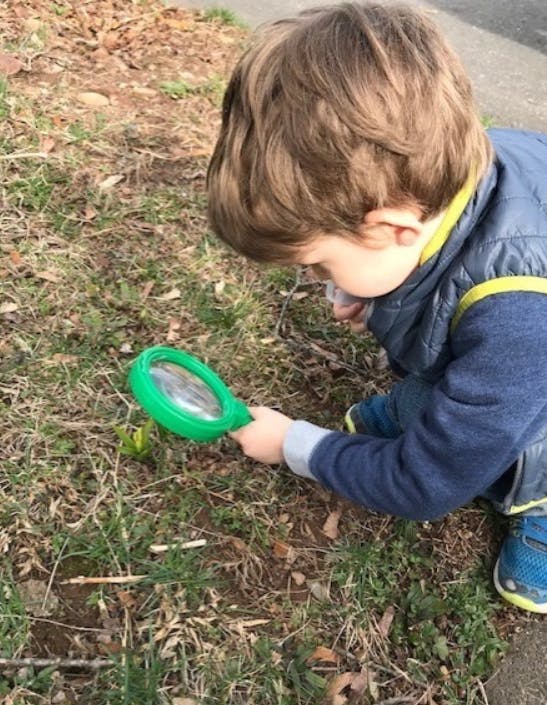 Child looking at ground with magnifying glass
