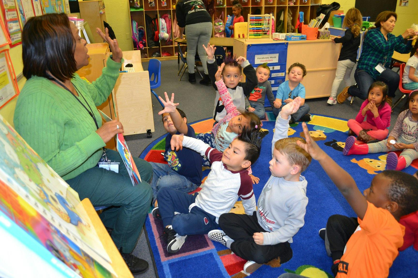 Adult reading to children in a classroom, children raising hands