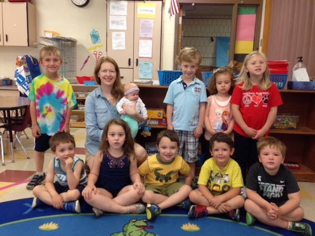 Adult holding an infant with a group of children in a classroom