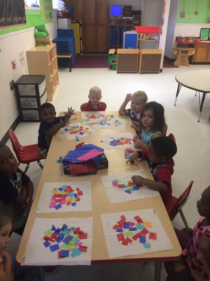 Children sitting at a table doing an art project with colorful paper squares