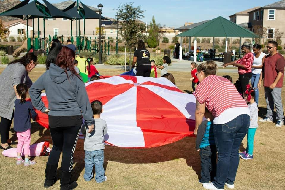 Adults and children playing with a large red and white parachute outdoors