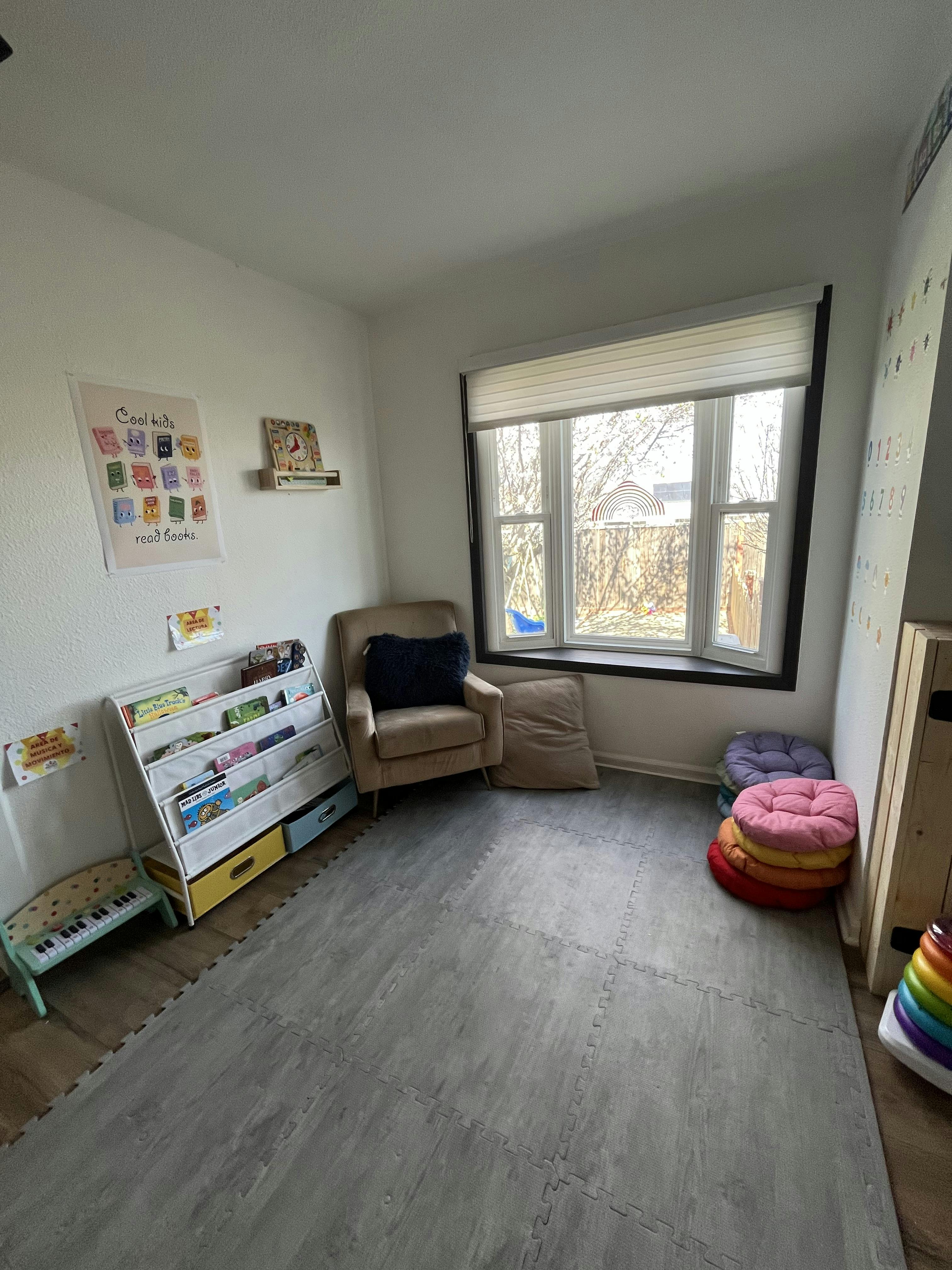 Children's room with book display, cushioned chair, window, and play mat