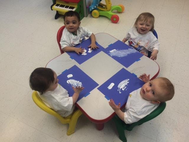 Four children sitting at a table with paint on blue paper