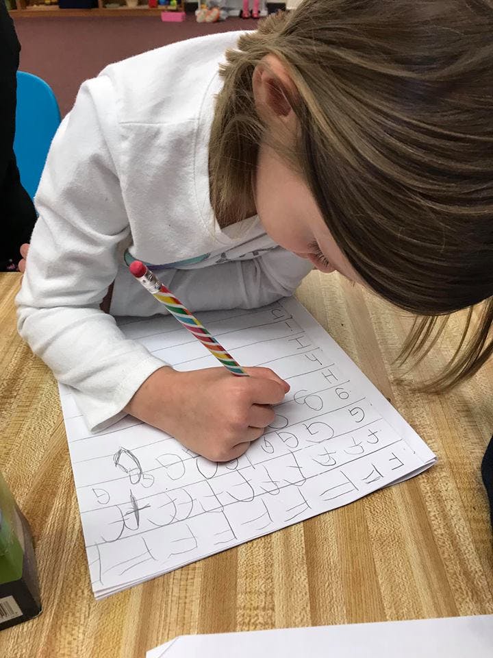Child writing letters on paper with a pencil