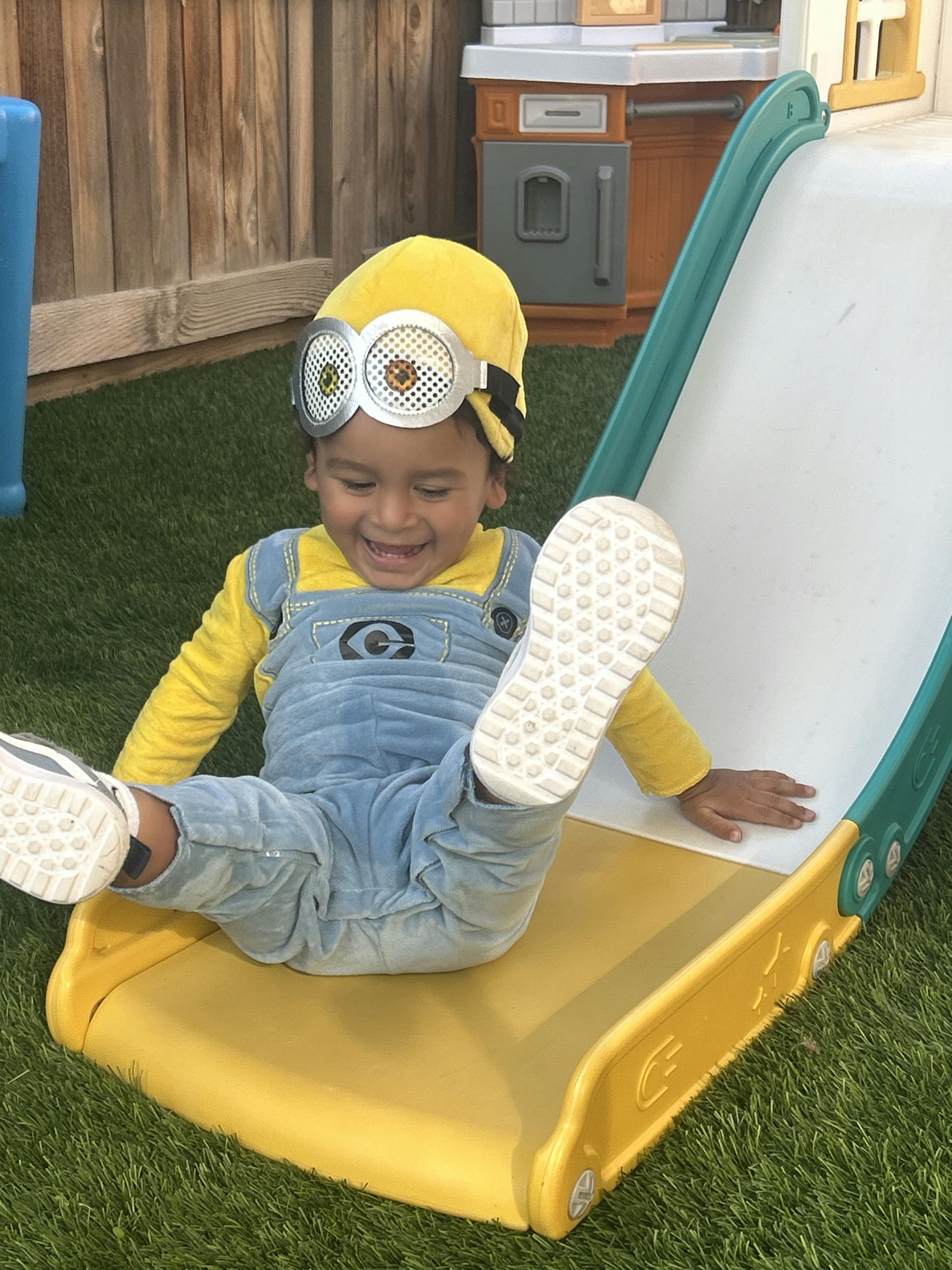 Child in overalls and goggles sitting at the bottom of a slide