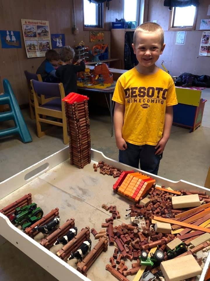 Child standing next to a tray of building blocks and toy animals