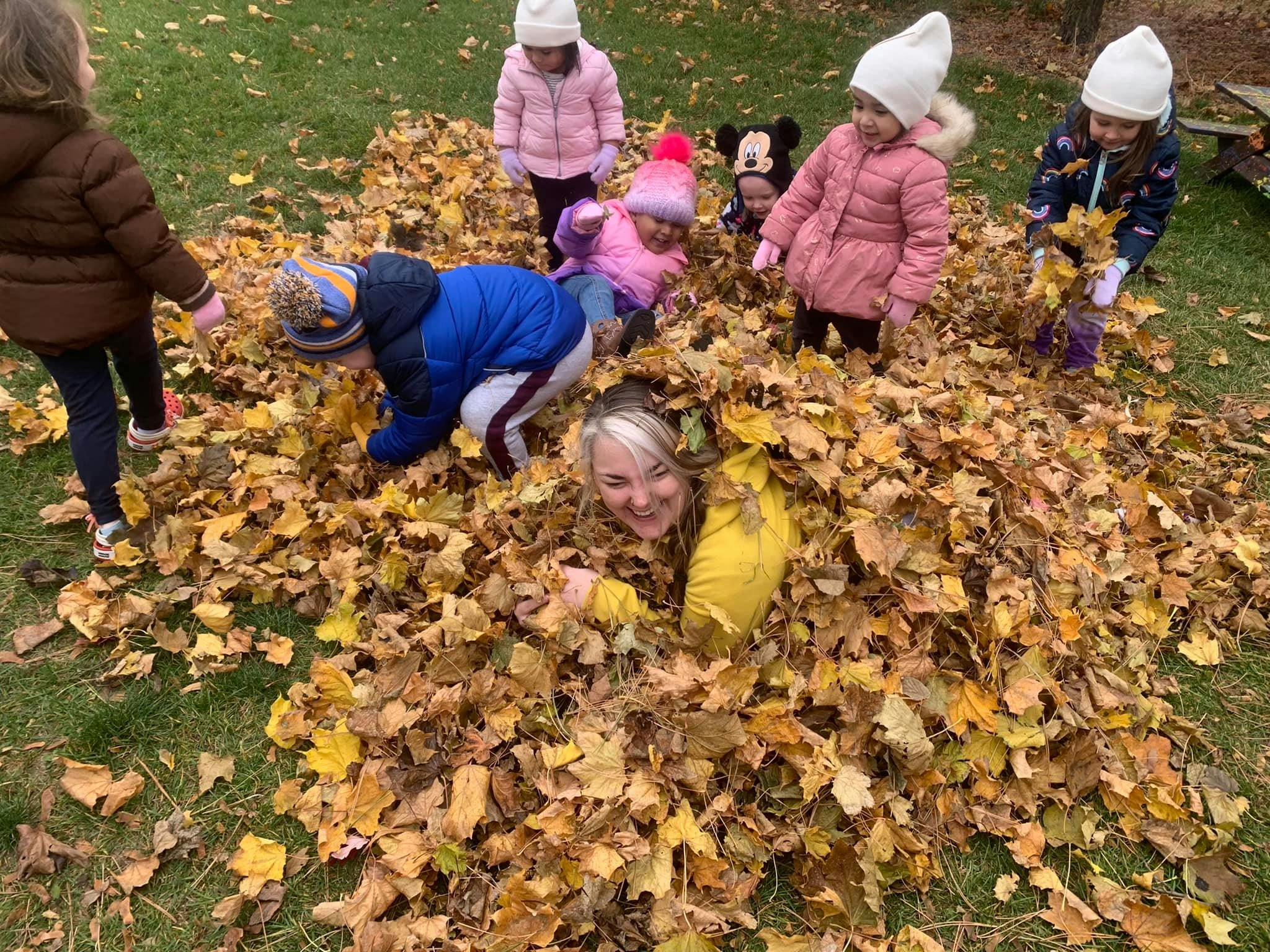 Person and children playing in a pile of autumn leaves