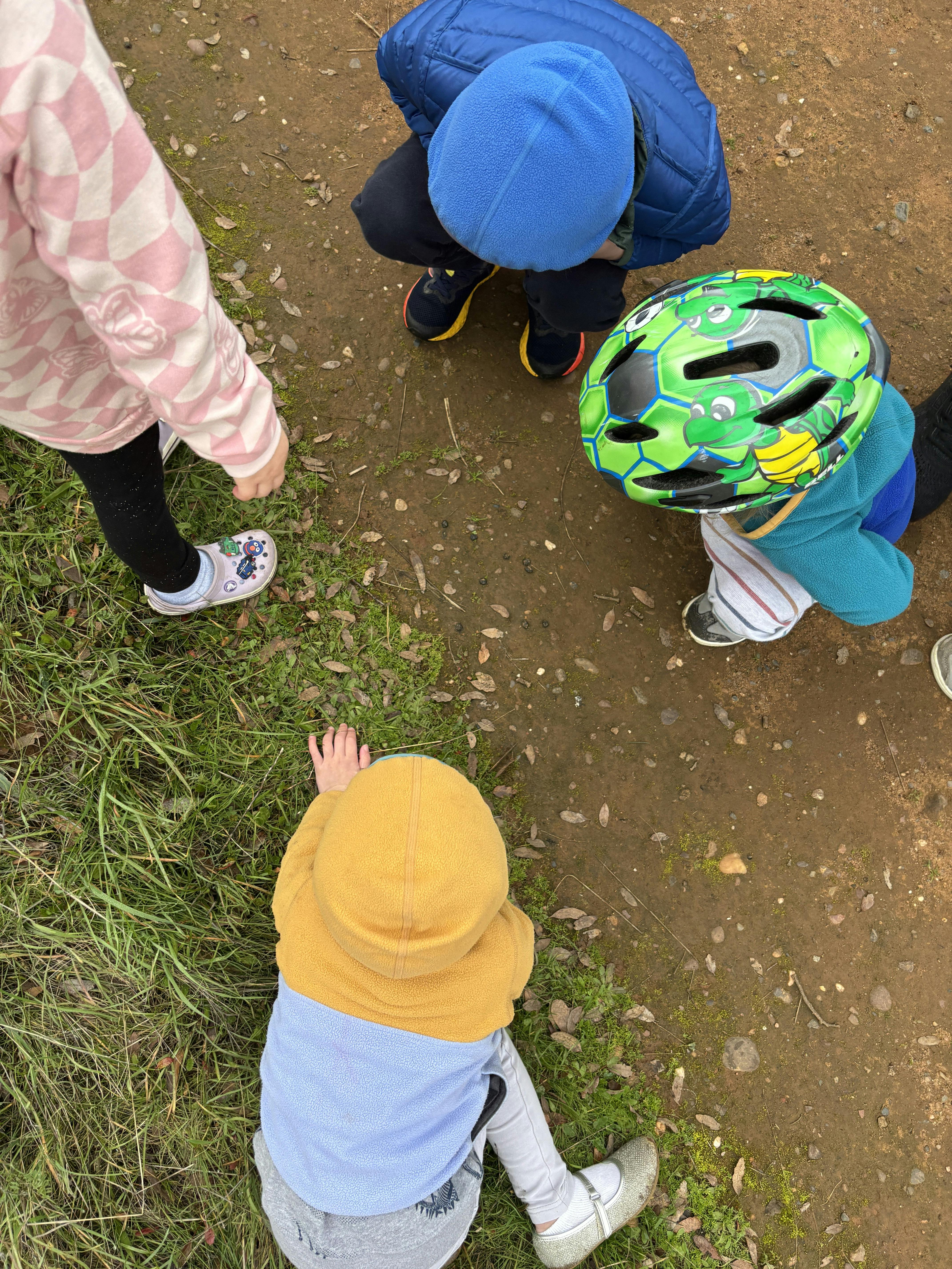 Three children crouching on a dirt path inspecting the ground
