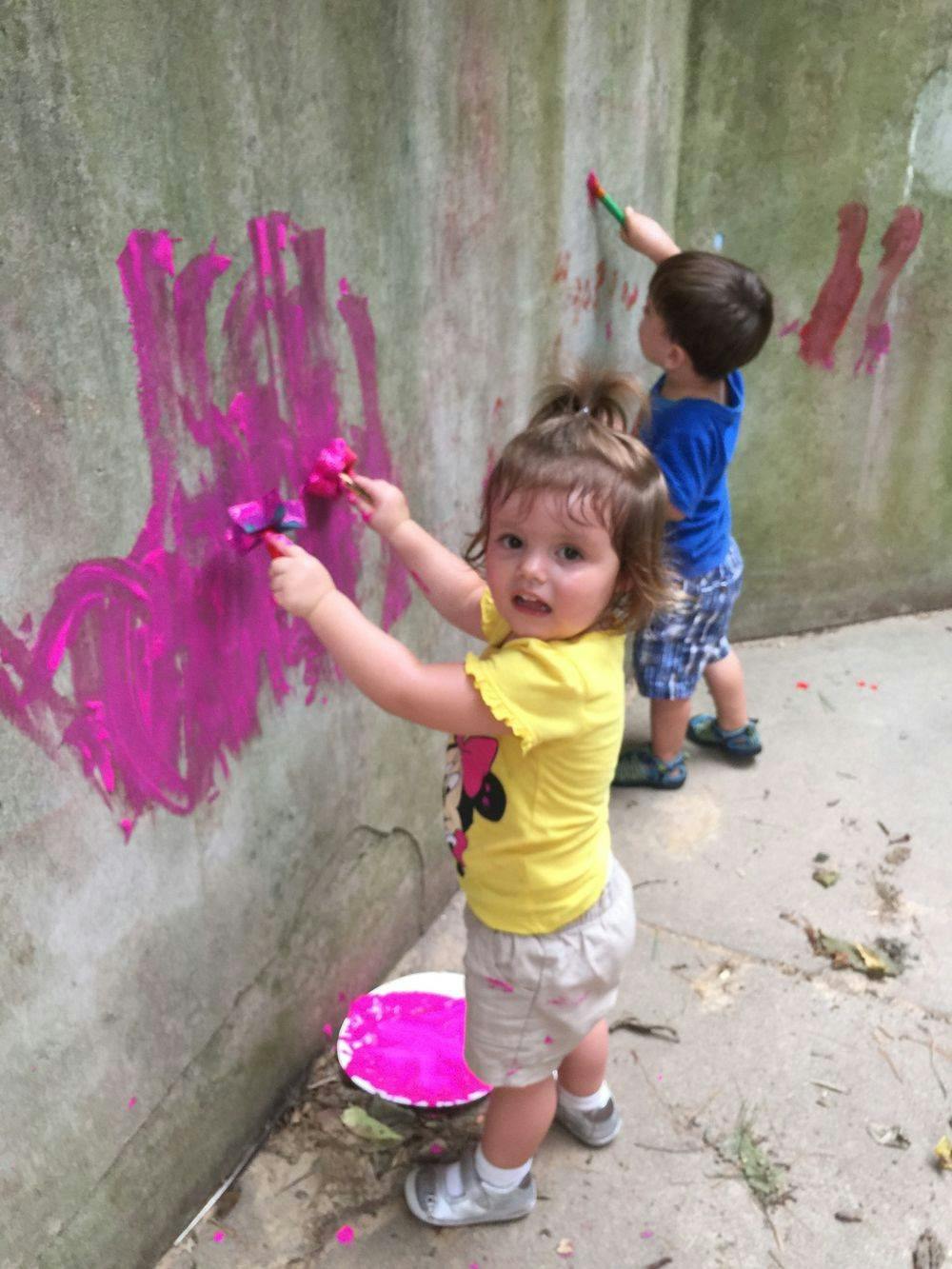 Two children painting a wall with pink paint